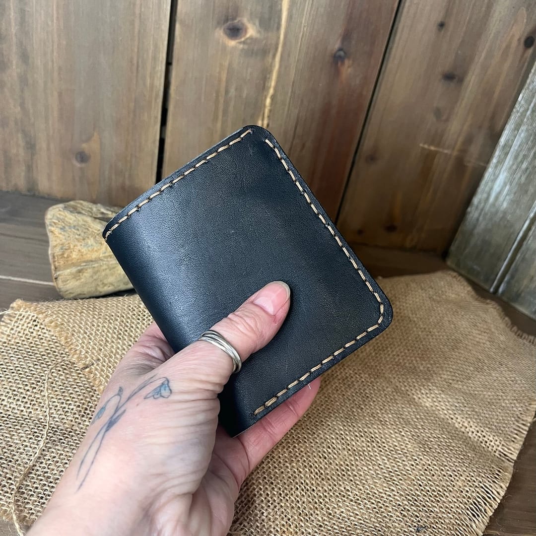 Black handmade leather bifold wallet held in hand